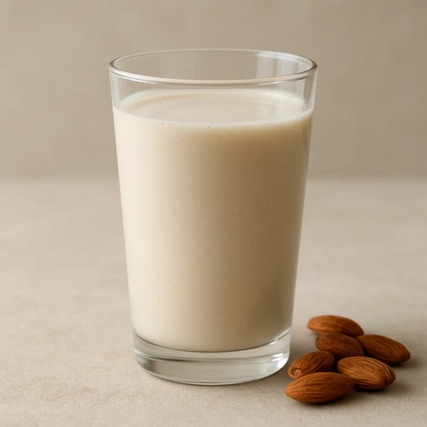 Creamy off-white mamra almond milk in a tall glass on a light stone surface