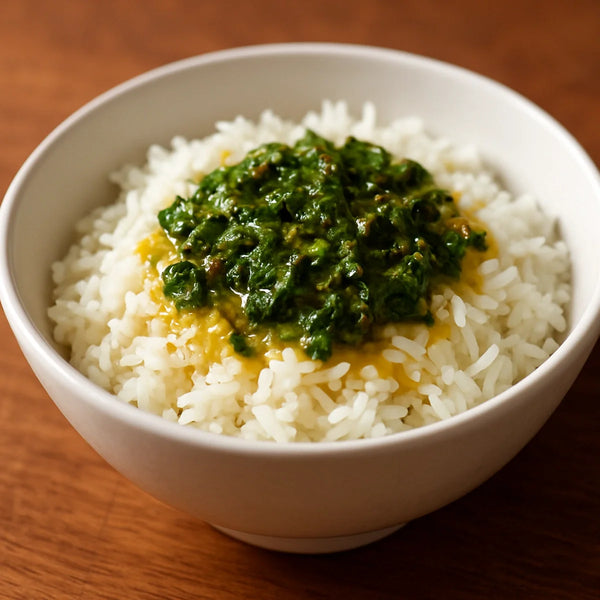 White rice in a ceramic bowl with vivid green moringa ghee tadka drizzled over the top