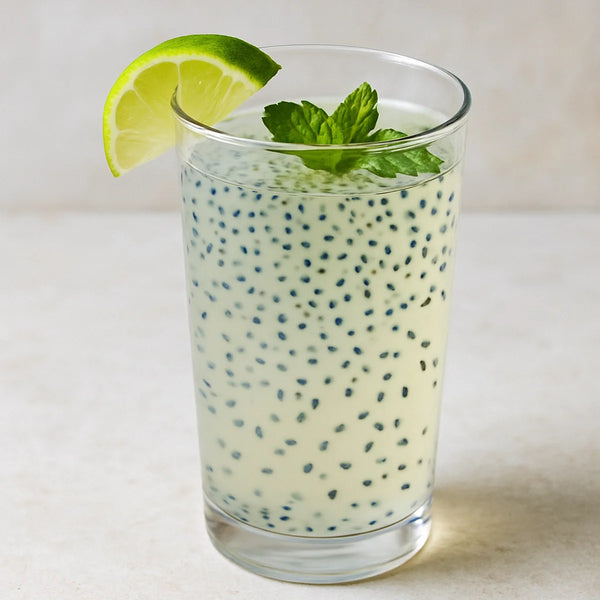 Pale coconut water sabja cooler in a tall glass with bloomed seeds, lime wedge and fresh mint leaves
