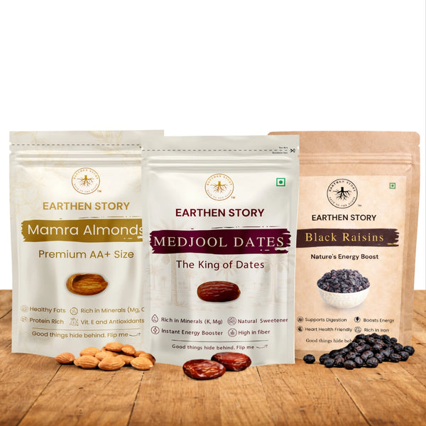 Dry Fruits Essentials Bundle with mamra almonds, medjool dates, and black raisins on a plain white background on a wooden desk.